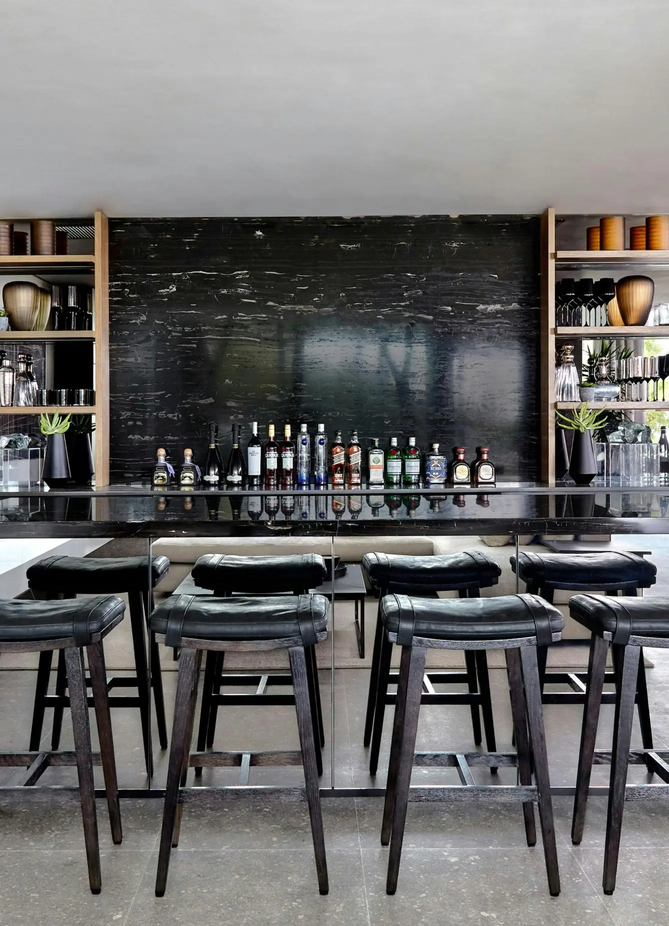 A bar area made out of black marble with 4 bar stools in the foreground and artwork to the left.